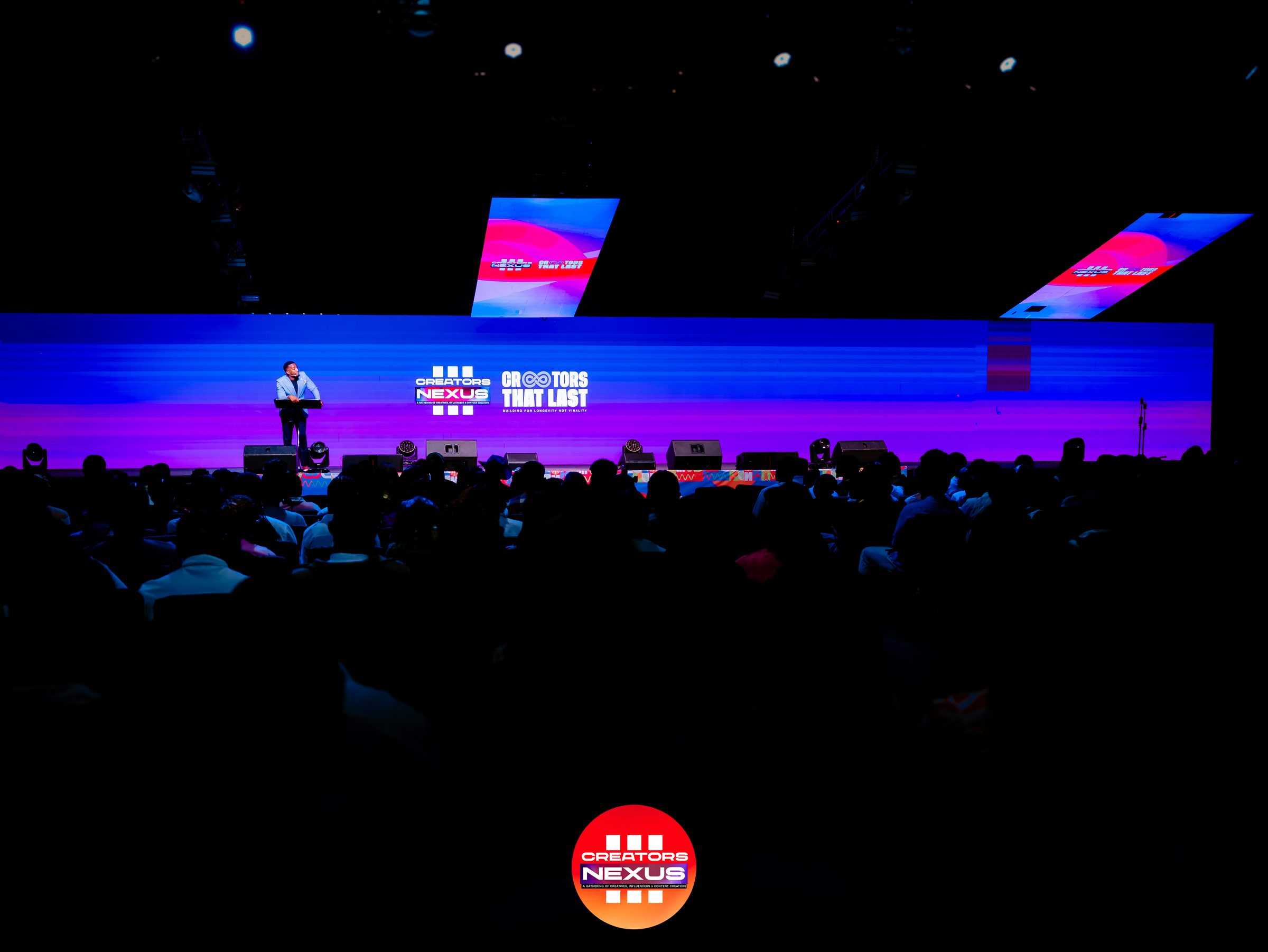 A speaker on stage at Creators Nexus, lit in purple and blue stage light.