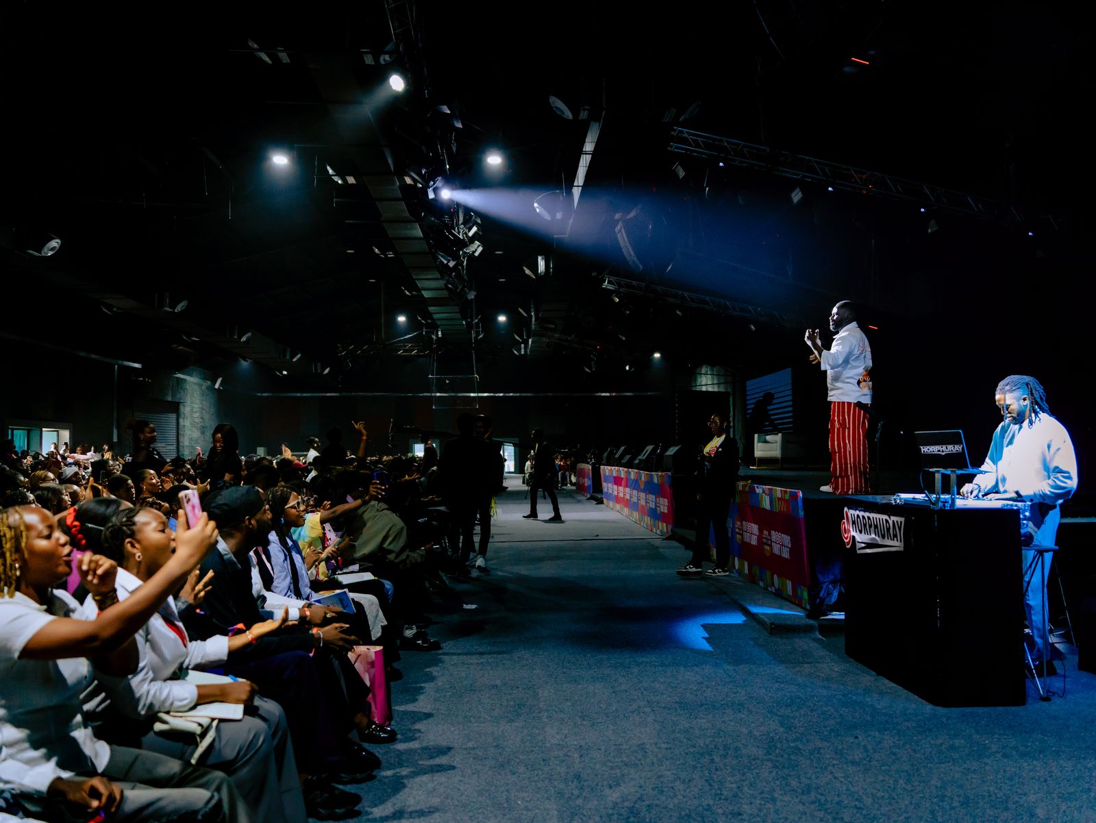 A performer on stage at Creators Nexus III, lit by a spotlight, with the crowd cheering in the foreground.